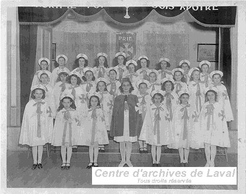 Groupe de jeunes filles sur une scne, en uniforme religieux blanc, arborant une croix.