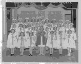 Groupe de jeunes filles sur une scène, en uniforme religieux blanc, arborant une croix.