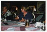 Deux femmes en discussions à une table avec des peintures en arrière-plan.
