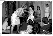 Groupe d'enfants sur une scène avec une dame qui donne un objet à une petite fille.