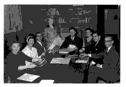Groupe de personnes (hommes et femmes) autour d'une table, photos à la main, lors d'une réunion.