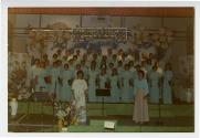 Groupe de personnes sur une scène et faisant partie d'une chorale et habillées d'un uniforme turquoise.