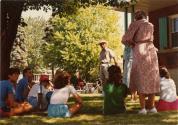 Journée cyclo-historique trajet ouest. Une dizaine de participants assis dans le gazon sous un arbre devant une maison. (22 juillet 1984)
