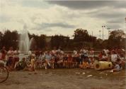 Rallye familial de vélo au Centre de la Nature. Groupe de familles assis aux tables devant le lac et la fontaine. (Août 1984)
