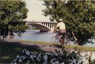 Randonnée cycliste. Un participant sur son vélo sur la piste cyclable sur le bord de la rivière ; on voit un pont également. [1987]