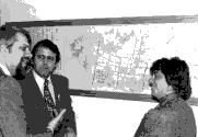 Jean-Guy Rodrigue discutant avec deux personnes non identifiées devant une carte géographique