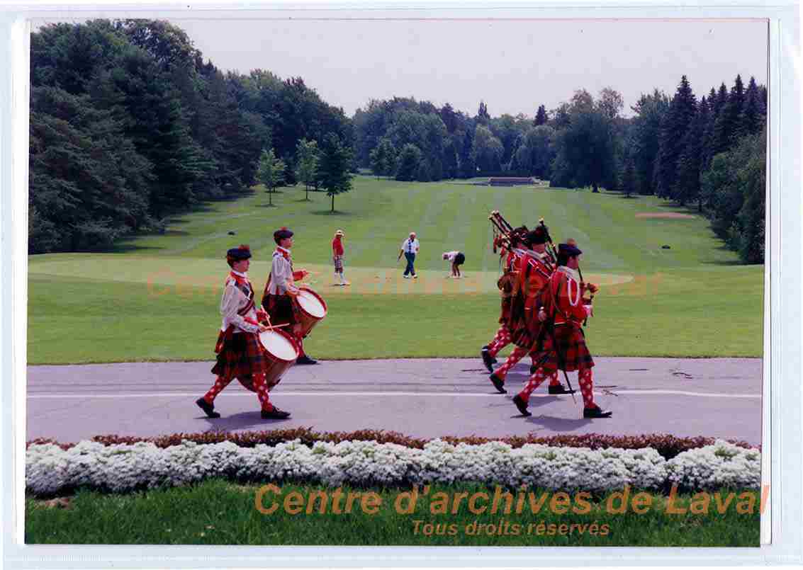 Groupe de musiciens en habits cossais jouant de la cornemuse et du tambour marchent sur une route du terrain de golf