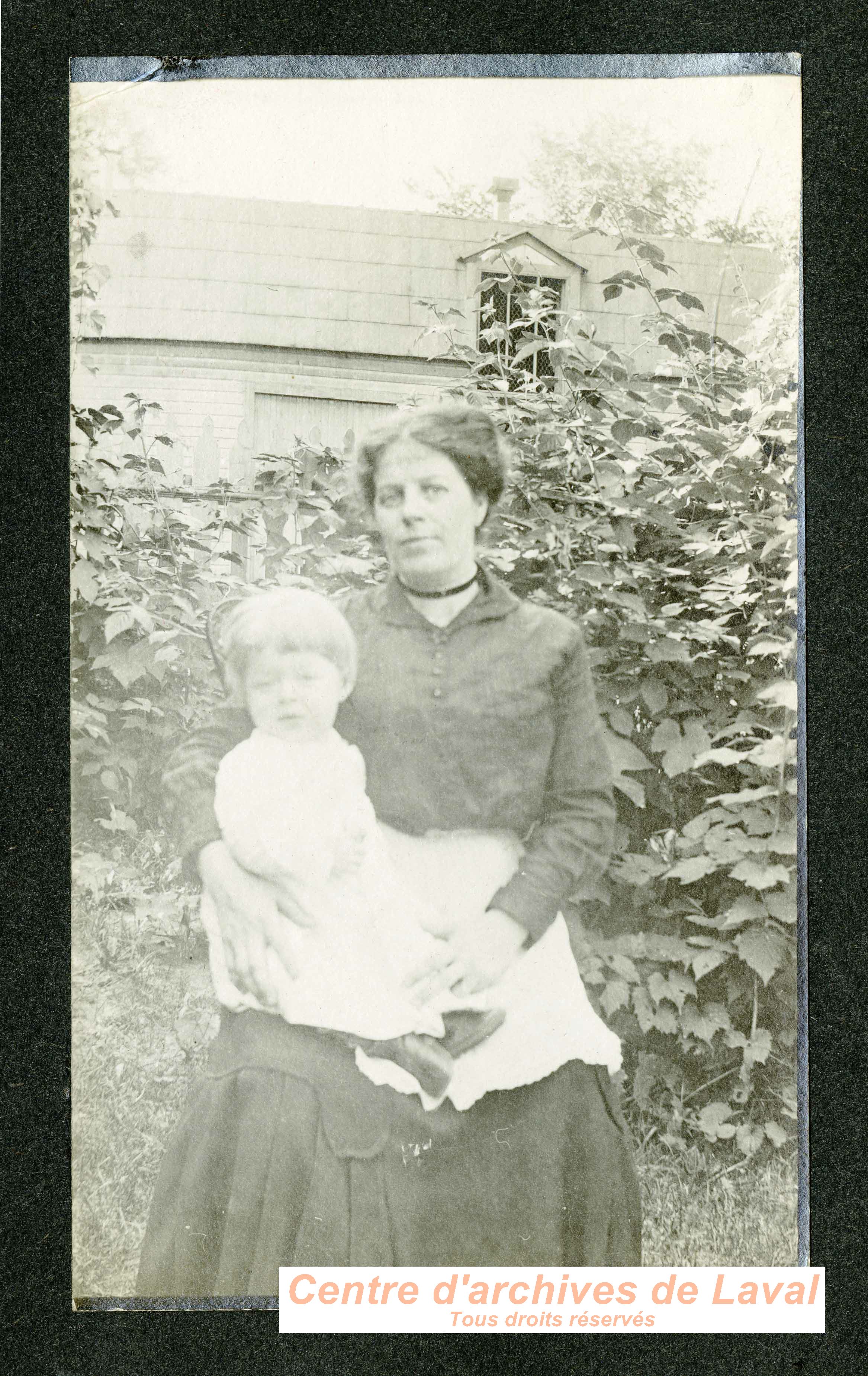 Femme tenant un enfant dans un jardin.